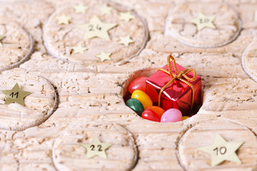 Advent calendar handmade from old timber with open window. Circular space filled with small gift and jelly beans. Calendar to count the days before Christmas. Medieval wood with wormholes. Macro photo