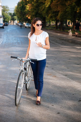 Attractive woman in sunglasses walking with bicycle and takeaway coffee