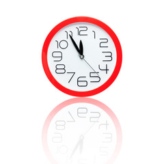 red alarm clock showing five minutes to midnight with reflection
