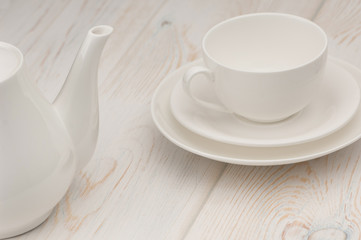 one white cup and saucer and a kettle on an old wooden board