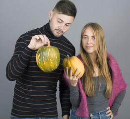 Young mand and girl holding pumpkins on grey background