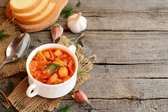 Cabbage soup with meat in a bowl, spoon, garlic, dill, pieces of bread on old wooden background with empty place for text. Soup cooked with meat, potatoes, cabbage, carrots, garlic, onion and tomato