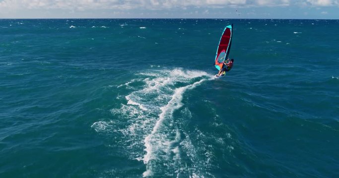 Aerial view of windsurfer gliding across blue ocean jumping off wave, extreme sport