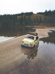 Miniature car is traveling around the world. Caricature car is wondering on the shore on a cloudy day. Ski resort in the background. Image has a vintage effect applied.