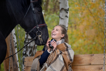 girl in a plaid with a black horse in the autumn under a birch tree on a bench