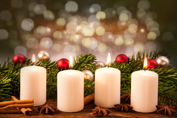 vier brennende Advent-Kerzen vor Weihnachtsschmuck im Tannenzweig