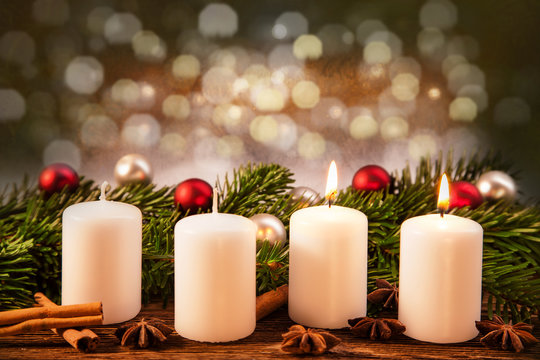 zwei brennende Advent-Kerzen vor Weihnachtsschmuck im Tannenzweig