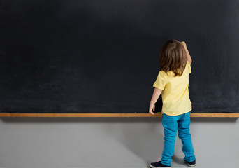 Child writing on blackboard, rear view.