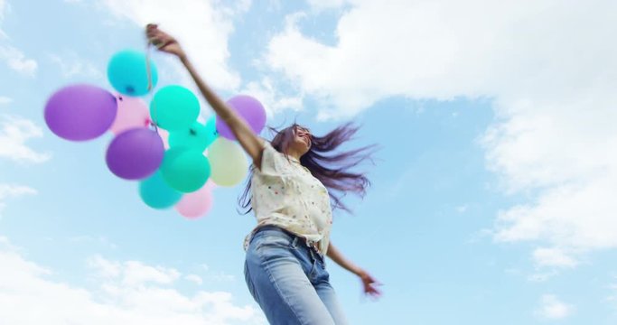 Beautiful young woman is running happy and carefree in a meadow with colorful balloons in hand all
