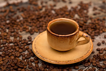 Small cup of coffee, roasted coffee beans on wooden background