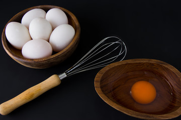 White Egg in small wooden teak bowl and whisk on black background