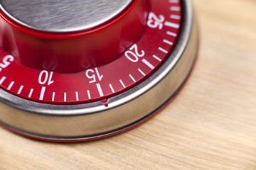 Macro view of a red kitchen timer showing 15 minutes on wooden b
