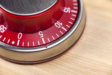 Macro view of a red kitchen timer showing 5 minutes on wooden ba