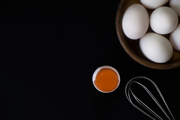 White Egg in small wooden teak bowl and whisk on black background