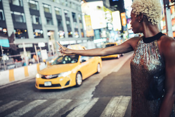 USA, New York City, young woman hailing a taxi on Times Square at night