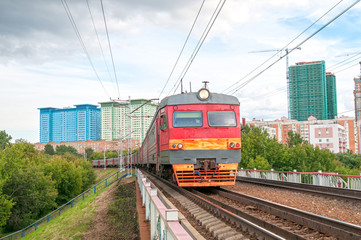 Red and grey suburban electric train moves towards on railroad turn vanishing against skyline background. Moscow, Russia. 
