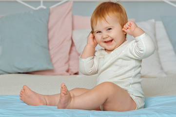 child touches ears by the hands,sits on a bed in a nursery