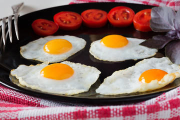 Fried quail eggs with tomatoes on a black plate