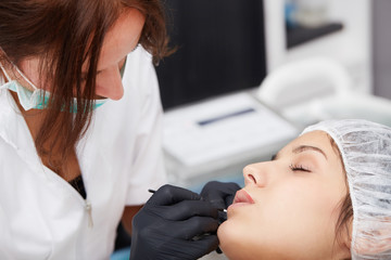 Obraz na płótnie Canvas Cosmetologist applying permanent make up on lips