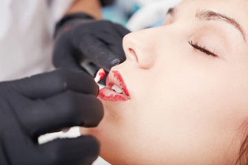 Cosmetologist applying permanent make up on lips