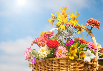 Fototapeta na wymiar Brilliant, colorful flowers in a wicker basket against sky and clouds