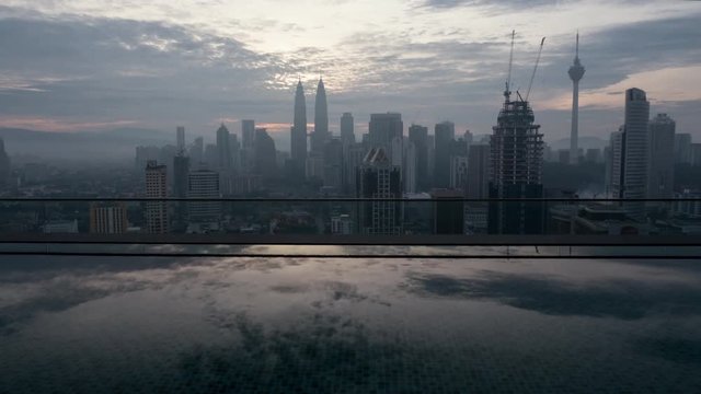 Timelapse shot of Kuala Lumpur city, view from rooftop pool. Panorama of Malaysia capital with clouds reflecting in water in foreground