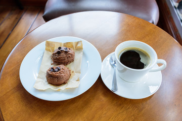 Black coffee cup with chocolate cookie on wooden background