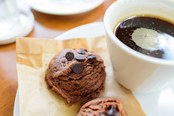 Black coffee cup with chocolate cookie on wooden background