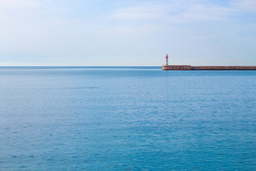 Calm sea and lighthouse at the end of the promenade.