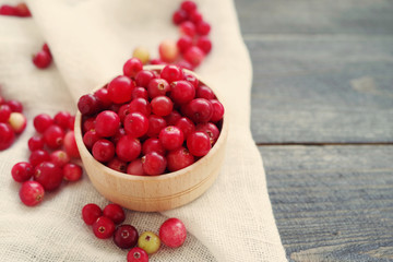 Fresh juicy cranberry in wooden round bowl with a wooden spoon on a table, top view