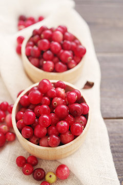 Fresh juicy cranberry in wooden round bowls with a wooden spoon on a table, top view