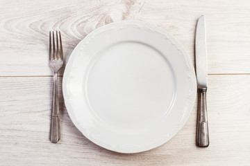 Plato blanco y cubiertos sobre mesa blanca de madera rústica