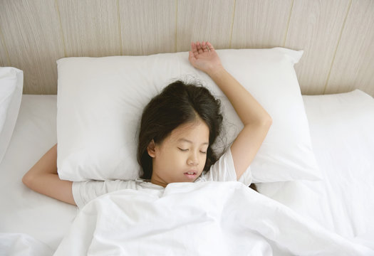 Portrait of happy young Asian girl with long black hair sleeping in bed at home.