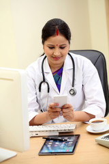 Young traditional female doctor texting at her desk