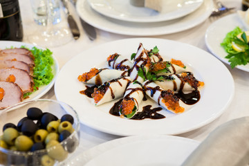 Pancakes with red caviar on a plate among the appetizers on the holiday table