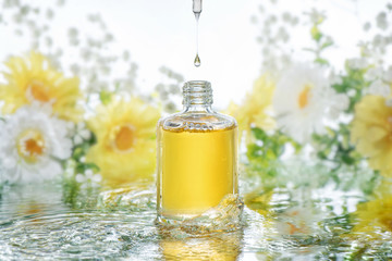 The bottle of moisturizing serum stands in the water waves on the nature blur flowers background....