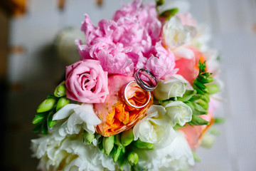 Wedding rings lie on the Bridal bouquet of roses and peonies. Wedding rings white gold