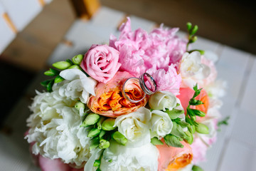 Wedding rings on a background of pink, white and orange peonies