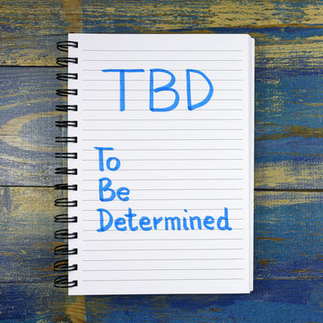 TBD- To Be Determined text written in notebook on wooden background