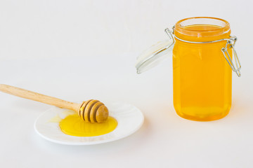 Jar with honey. Нoney dipper on white saucer.