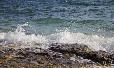 Wave with splash and foam crest drops to seashore's stone.