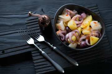 Calamari, octopus and potato salad on a black wooden surface