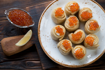 Rolled crepes topped with sour cream and salmon caviar