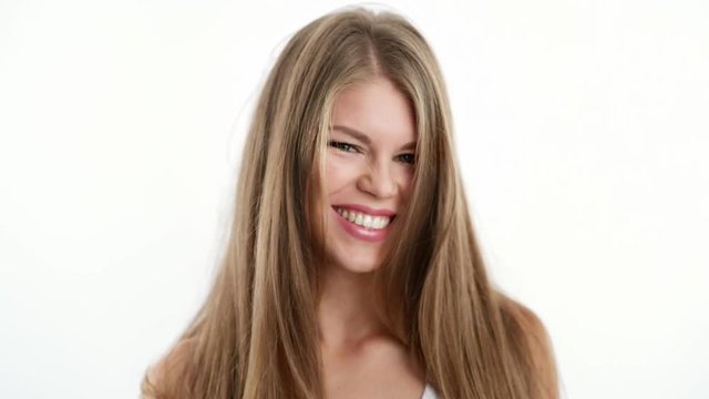 Pretty smiling female model touching her long straight shiny hair over bright background. Concept of hair care and cosmetics.