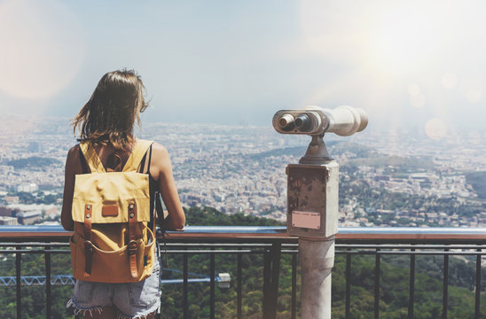 Hipster young girl with bright backpack looking on observation deck and travel plan. Tourist traveler background panoramic view of city, coin binoculars. Mock up for text message. Barcelona Tibidabo