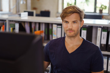 Fototapeta premium mann sitzt am schreibtisch im büro und schaut auf seinen computer