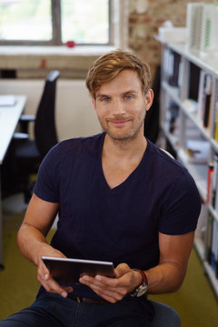 mann sitzt im büro am schreibtisch und hält sein tablet in der hand