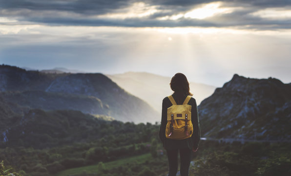 Hipster young girl with bright backpack enjoying sunset on peak of foggy mountain. Tourist traveler on background valley landscape view mockup. Hiker looking sunlight flare in trip Picos de Europa