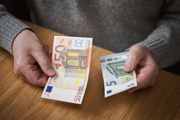 an elderly man holding a euro denomination banknotes of 50 and 5 Euro