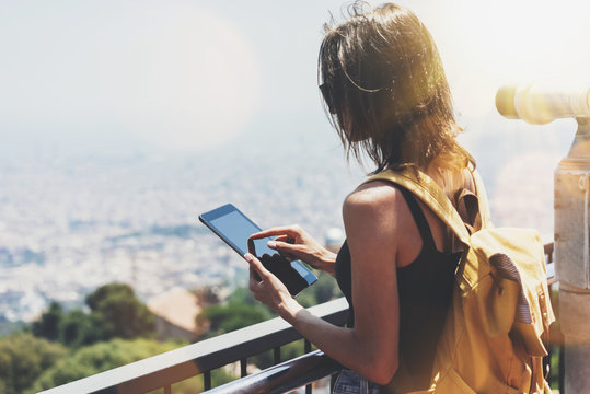 Hipster girl with backpack holding gadget in observation view. Tourist traveler on background panoramic city Barcelona, female hands using tablet and map, operated binoculars wich sun flare, mockup